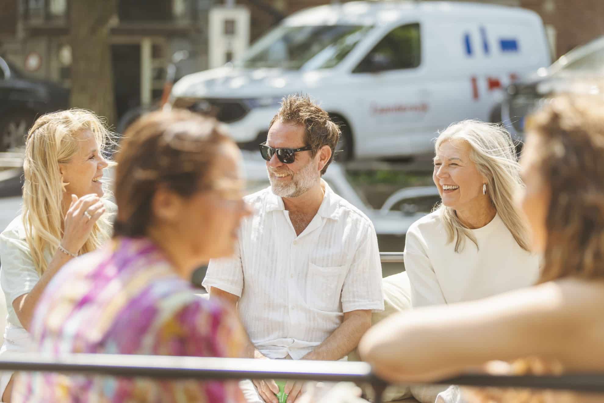 Een groep mensen zit gezellig samen op een boot in Amsterdam, lachend en pratend terwijl ze genieten van de rondvaart.