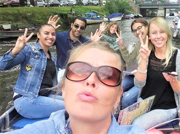 Vriendengroep op een bootje op de Amsterdamse grachten met de handen in lucht.