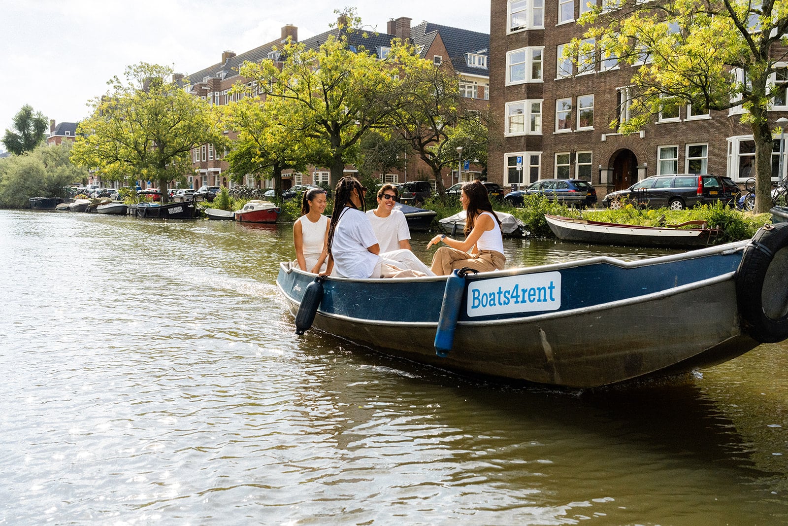 Boaty/Boat4Rent Drei Frauen und ein Mann segeln auf einem Boot durch die Amsterdamer Grachten.