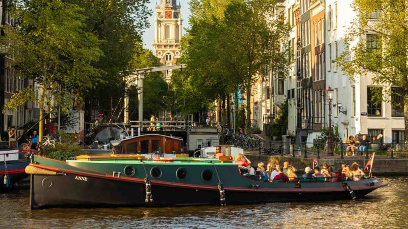 Classic tugboat during sunset on the Amsterdam canals with a group of people.