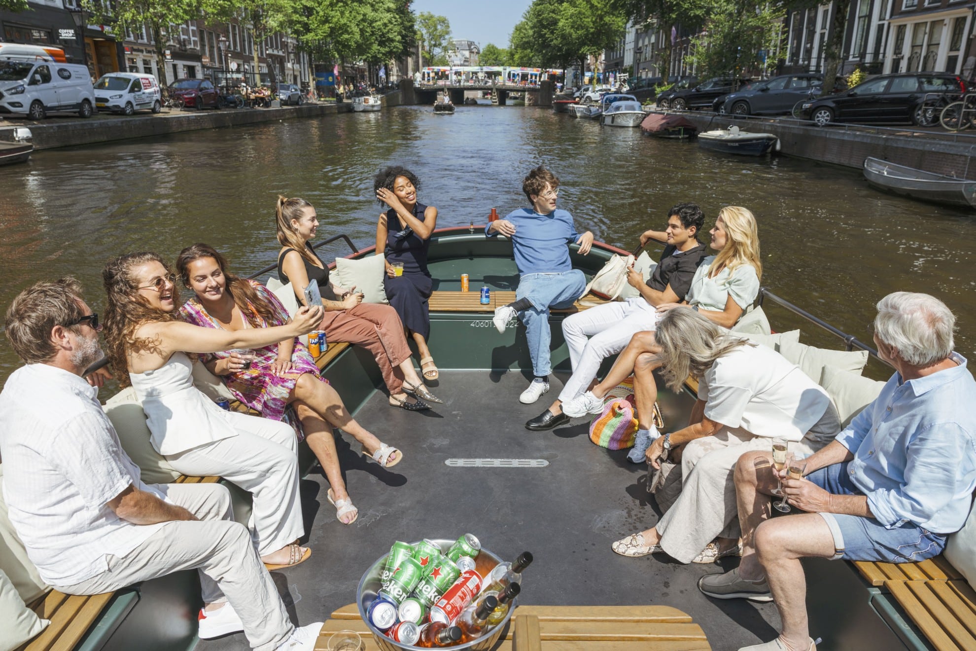 Bootjehureninamsterdam.com – Groep mensen op de klassieke sleepboot Eine Gruppe von Menschen genießt eine sonnige Kreuzfahrt durch die Amsterdamer Grachten, plaudert, trinkt und macht Selfies auf dem Boot.